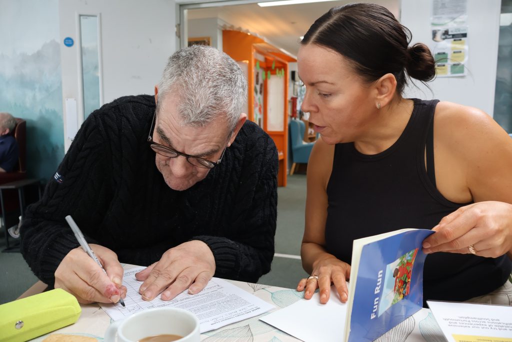 An SSJ support worker and a man working through a reading book together